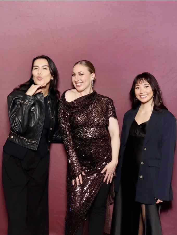 Three guests posing in front of a wine-red photo booth backdrop, one blowing a kiss