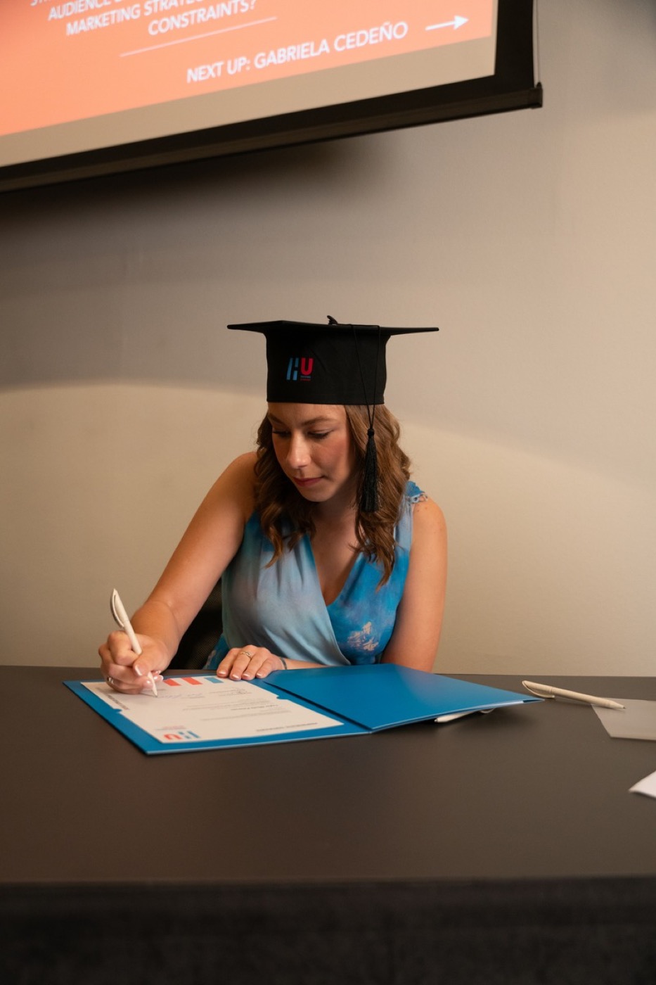 Taylor in an HU graduation cap signing the diploma