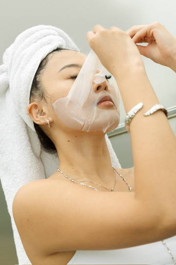 Model peeling off a sheet mask, head wrapped in a towel