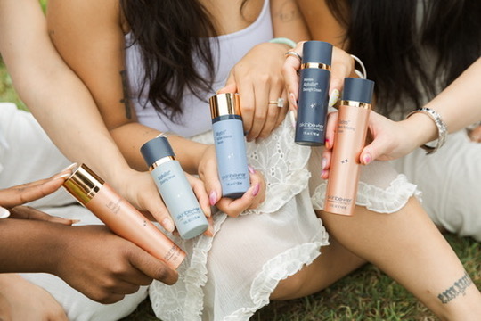 Hands holding skincare bottles over a white lace skirt on the grass