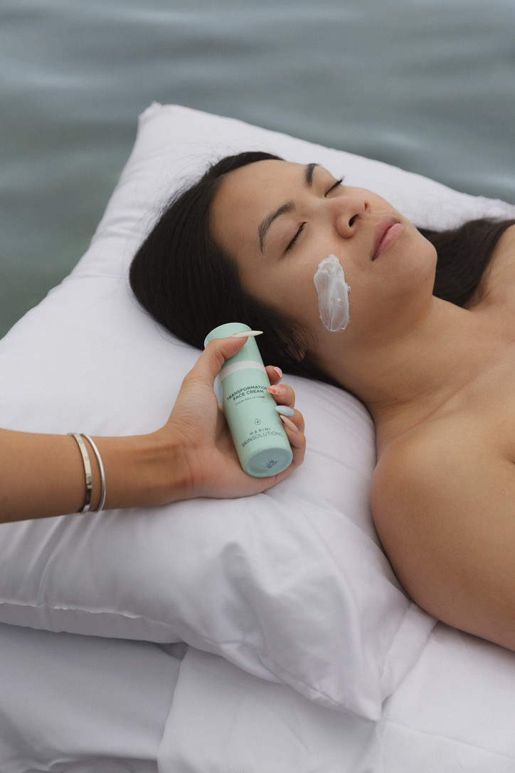 Face cream applied to a model resting on a pillow beside the water