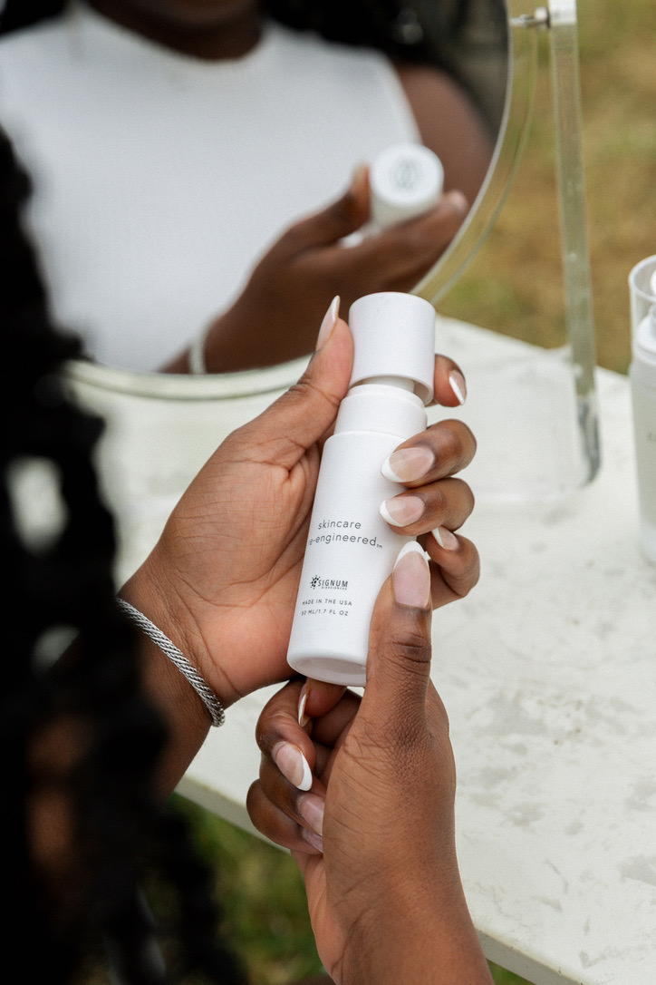 Hands holding a white skincare bottle in front of a vanity mirror