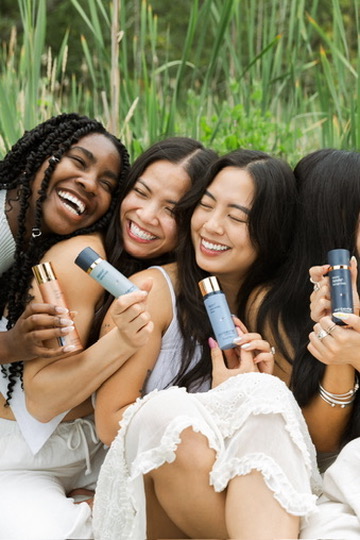 Four friends laughing together, each holding a skincare product