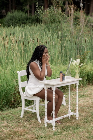 Model at a white vanity table in a meadow of tall grass