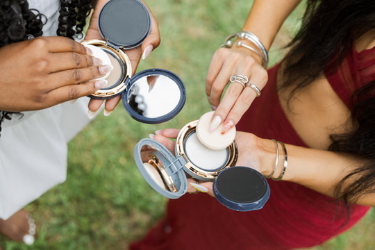 Hands holding open compacts above the grass