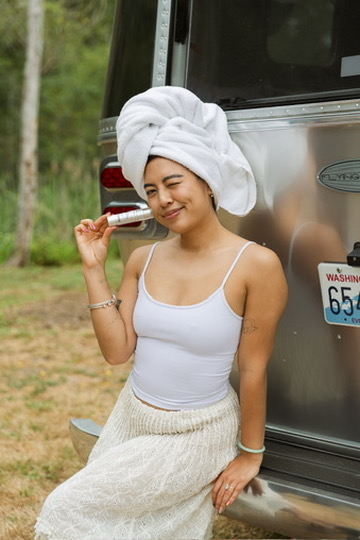 Model in a towel turban winking and holding a product beside an Airstream