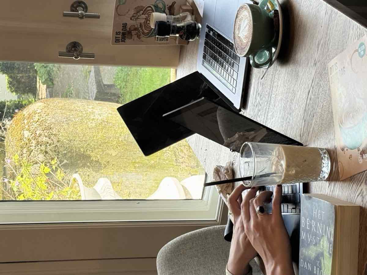 Laptops, an iced coffee and a cappuccino on a café table by a canal-side window